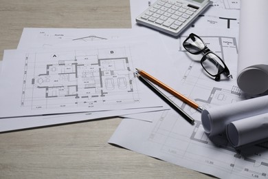 Photo of Different architectural drawings, calculator, glasses and pencils on wooden table, closeup