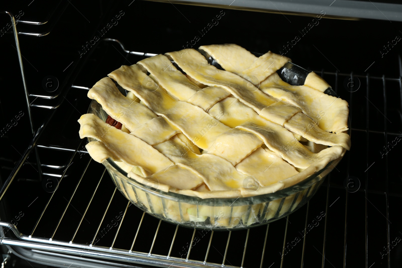 Photo of Baking dish with raw homemade apple pie in oven, closeup