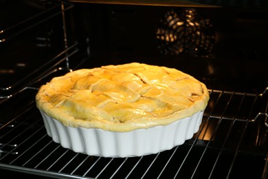 Photo of Baking dish with raw homemade apple pie in oven, closeup