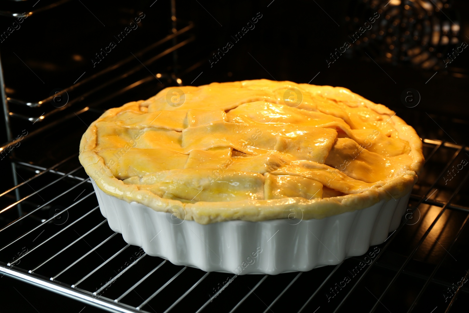 Photo of Baking dish with raw homemade apple pie in oven, closeup