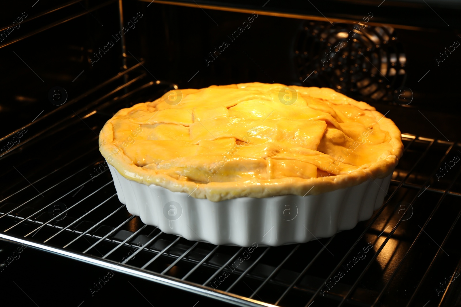 Photo of Baking dish with raw homemade apple pie in oven, closeup