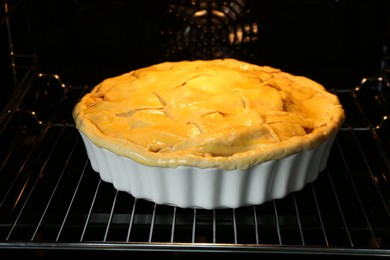 Photo of Baking dish with raw homemade apple pie in oven, closeup