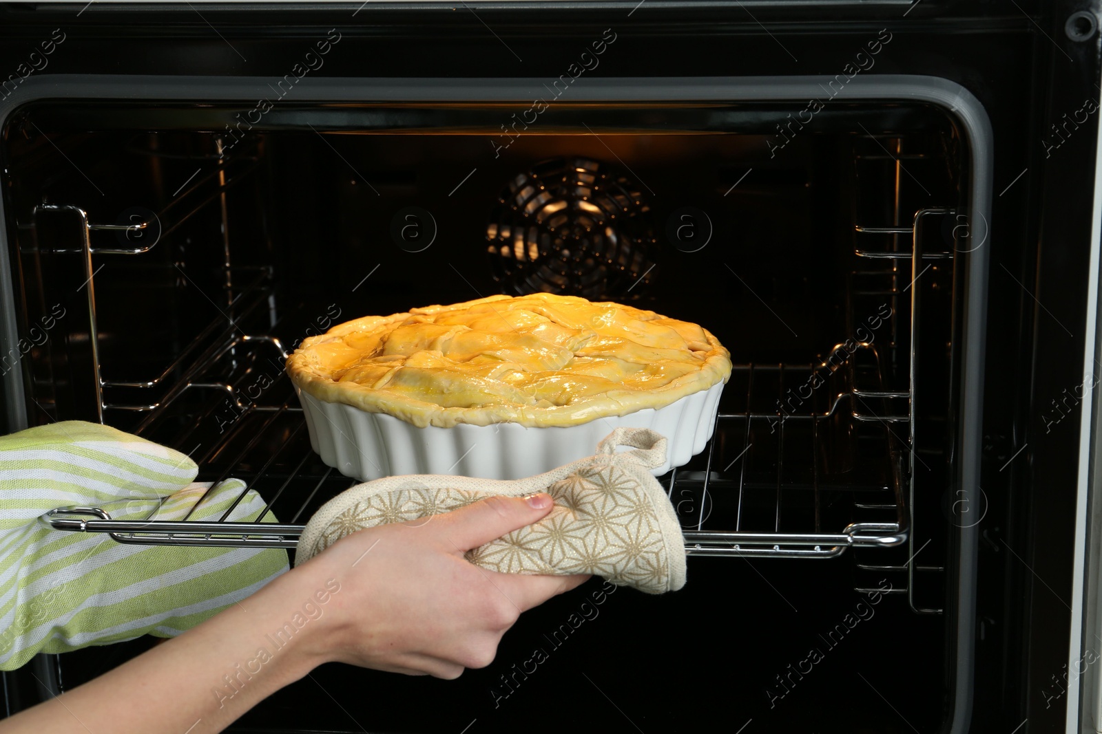 Photo of Woman putting homemade apple pie into oven in kitchen, closeup