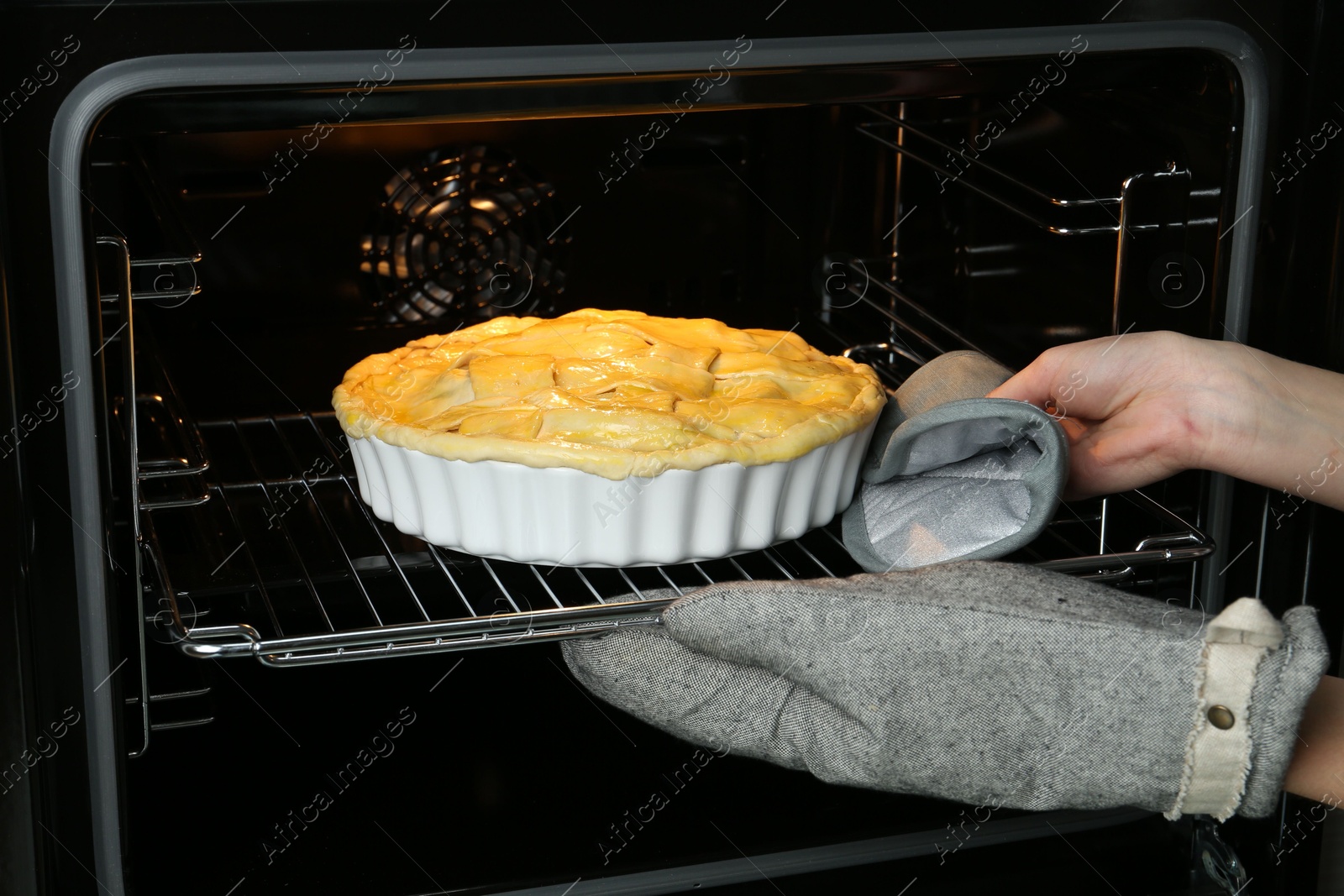 Photo of Woman putting homemade apple pie into oven in kitchen, closeup