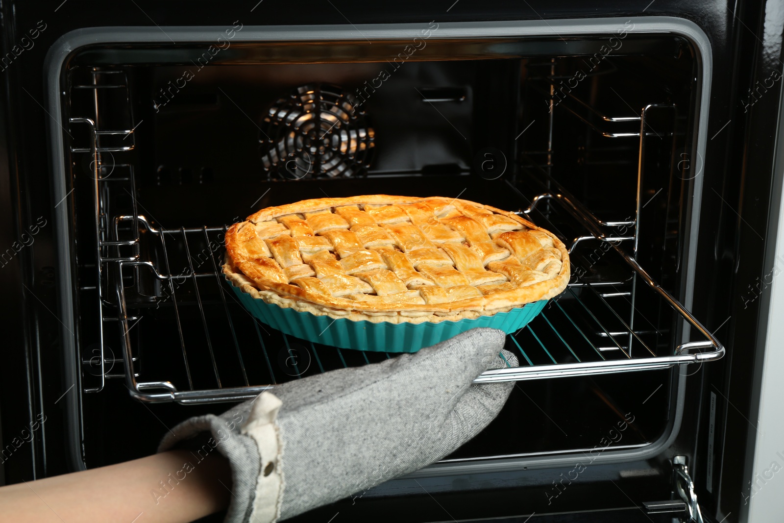 Photo of Woman taking delicious homemade apple pie out of oven in kitchen, closeup