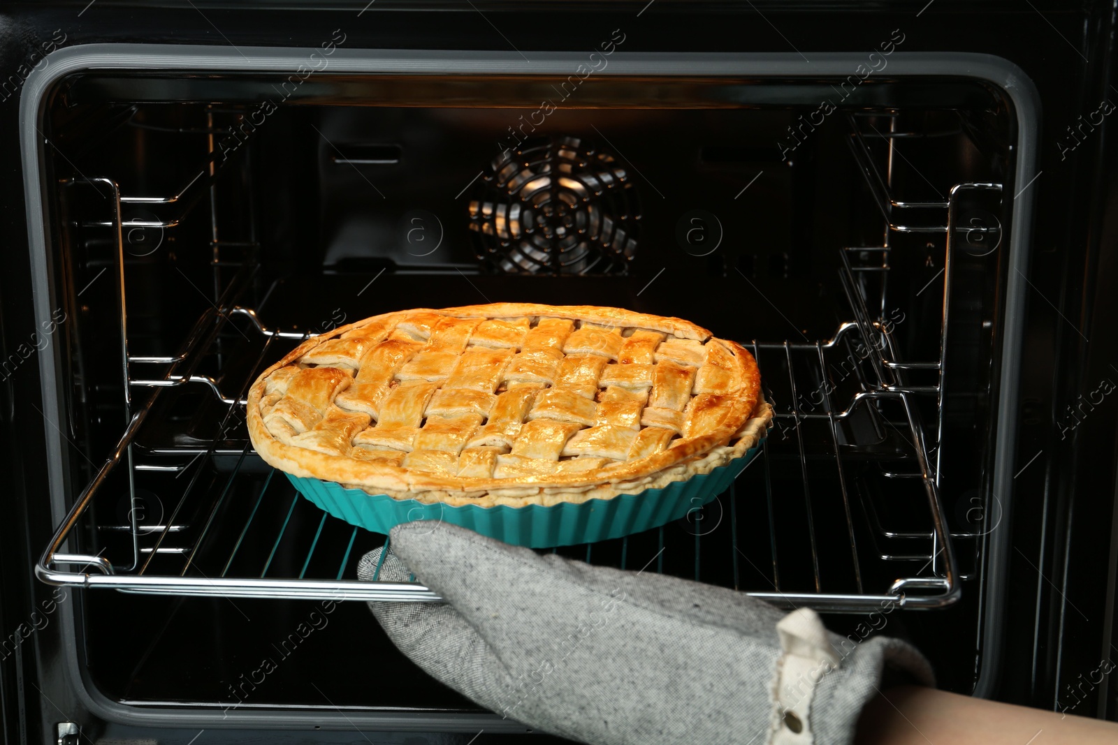 Photo of Woman taking delicious homemade apple pie out of oven in kitchen, closeup