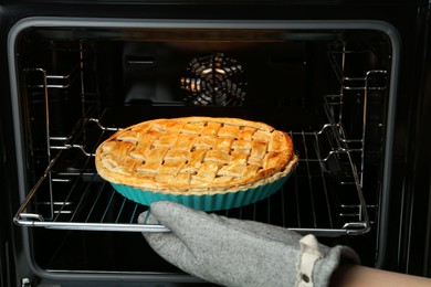 Photo of Woman taking delicious homemade apple pie out of oven in kitchen, closeup