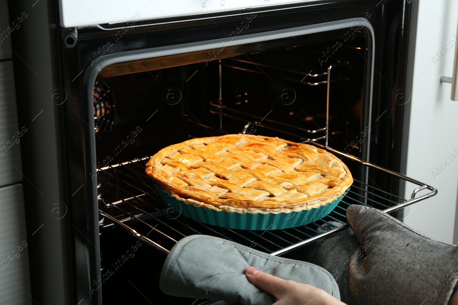 Photo of Woman taking delicious homemade apple pie out of oven in kitchen, closeup