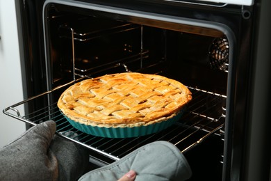 Photo of Woman taking delicious homemade apple pie out of oven in kitchen, closeup