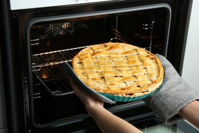 Photo of Woman taking delicious homemade apple pie out of oven in kitchen, closeup