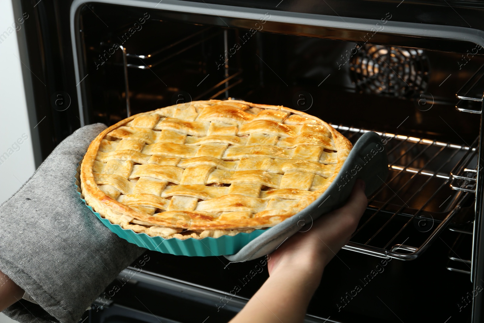 Photo of Woman taking delicious homemade apple pie out of oven in kitchen, closeup