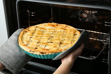 Photo of Woman taking delicious homemade apple pie out of oven in kitchen, closeup