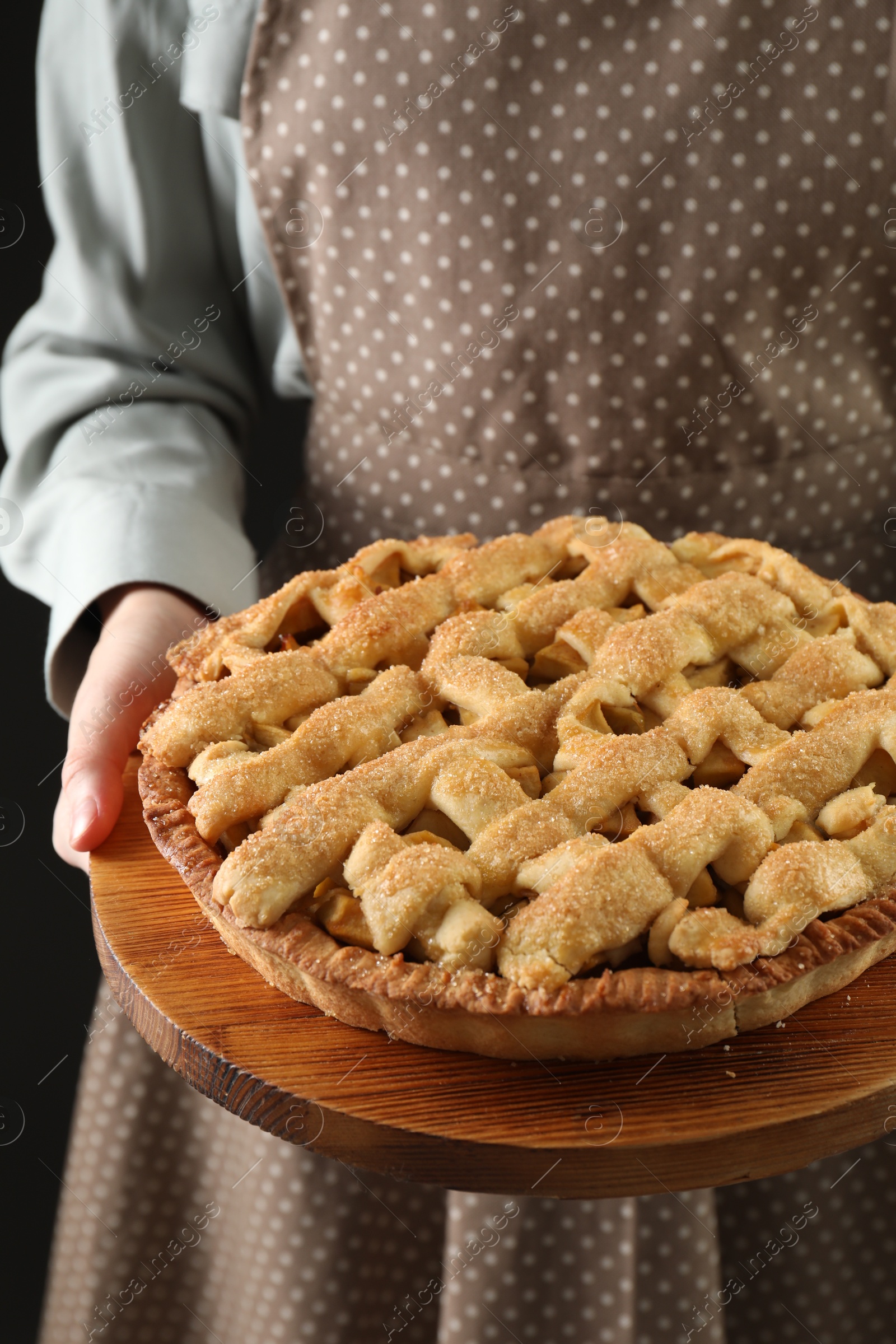 Photo of Woman holding wooden board with tasty homemade apple pie on black background, closeup