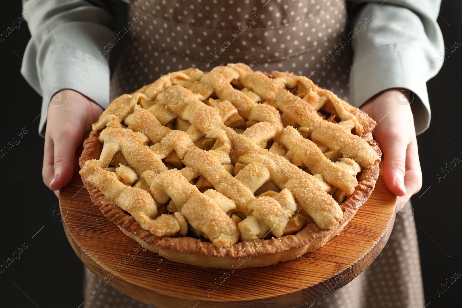 Photo of Woman holding wooden board with tasty homemade apple pie on black background, closeup