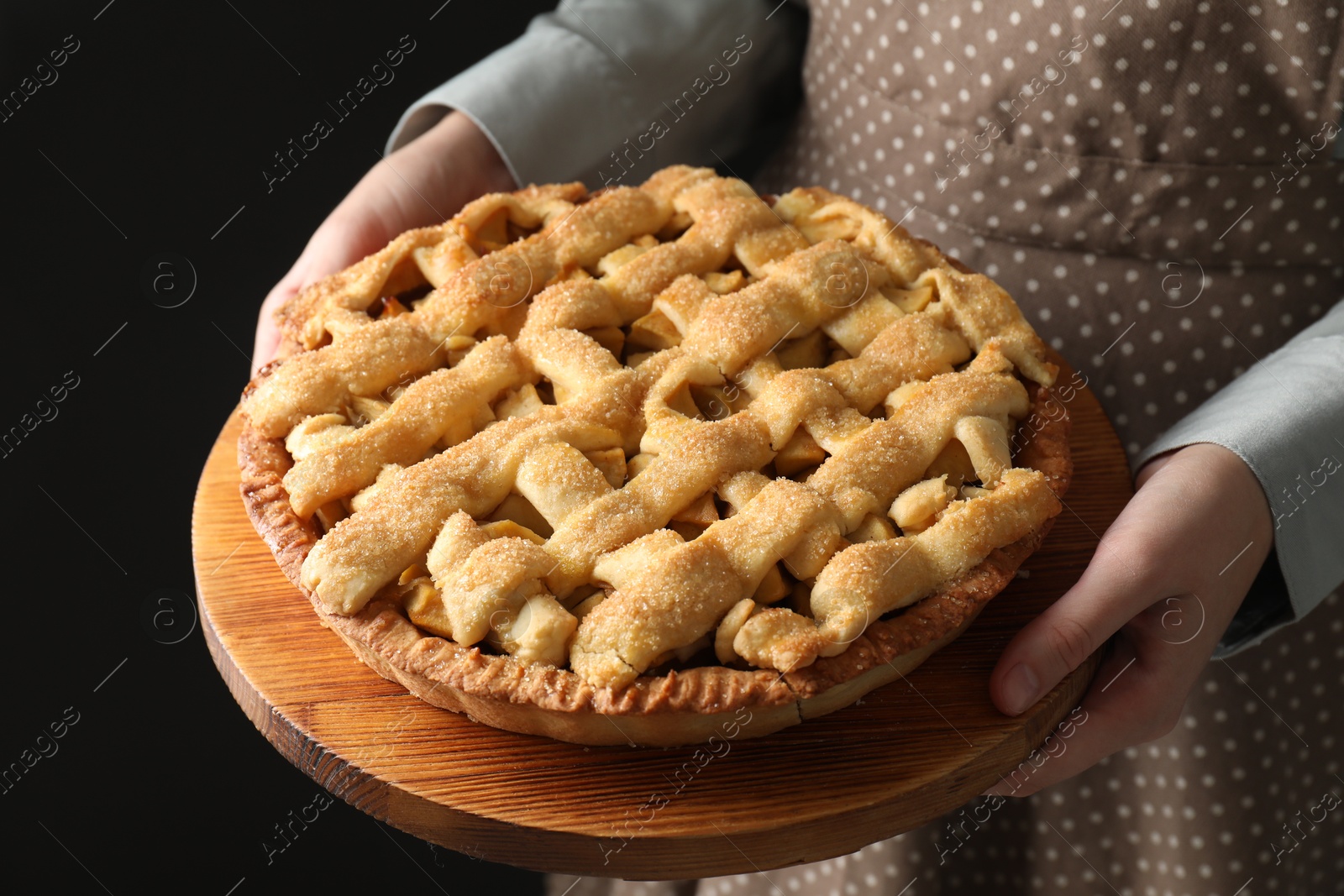 Photo of Woman holding wooden board with tasty homemade apple pie on black background, closeup