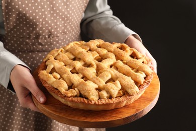 Photo of Woman holding wooden board with tasty homemade apple pie on black background, closeup