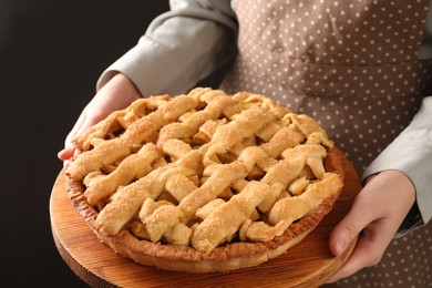 Photo of Woman holding wooden board with tasty homemade apple pie on black background, closeup