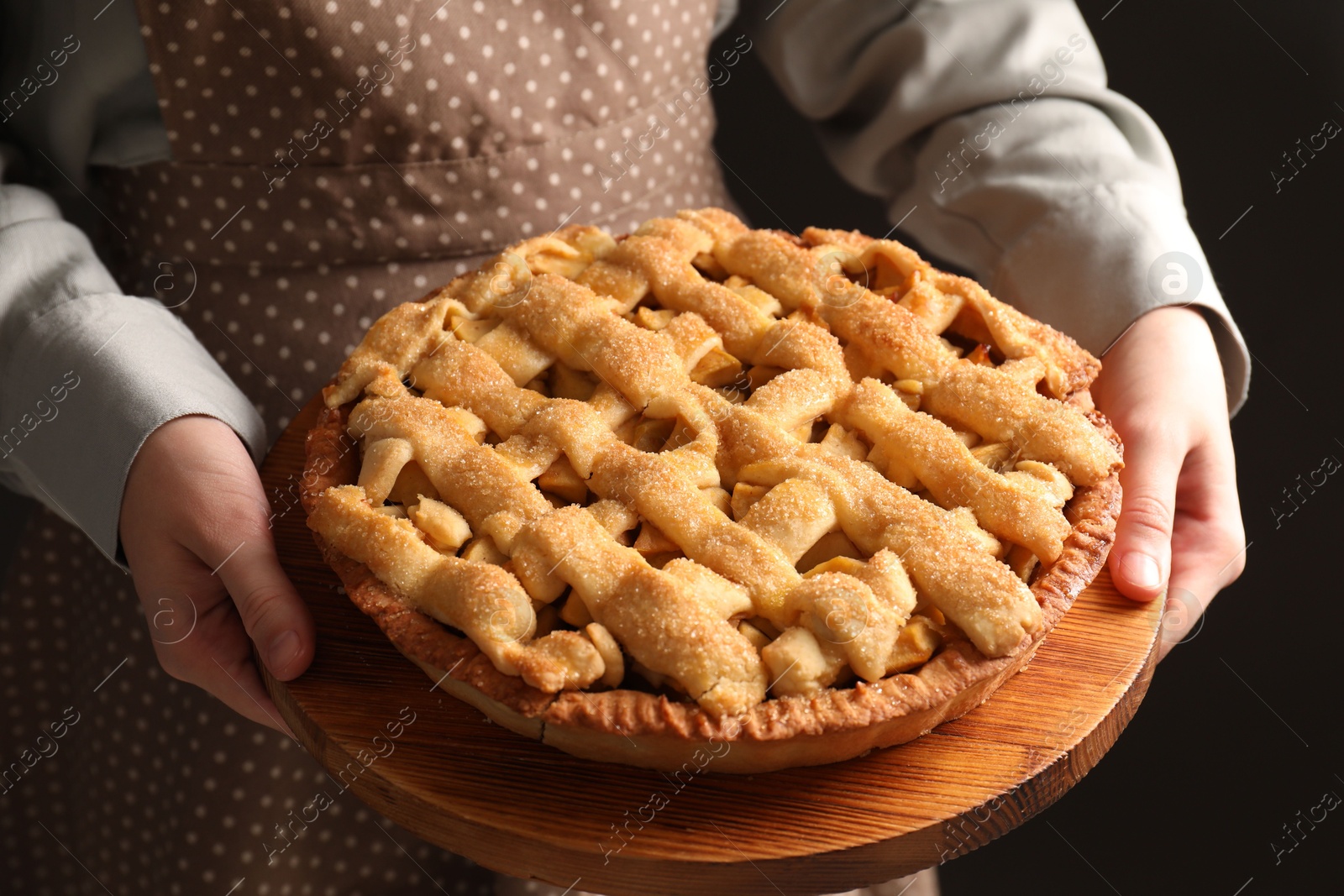 Photo of Woman holding wooden board with tasty homemade apple pie on black background, closeup