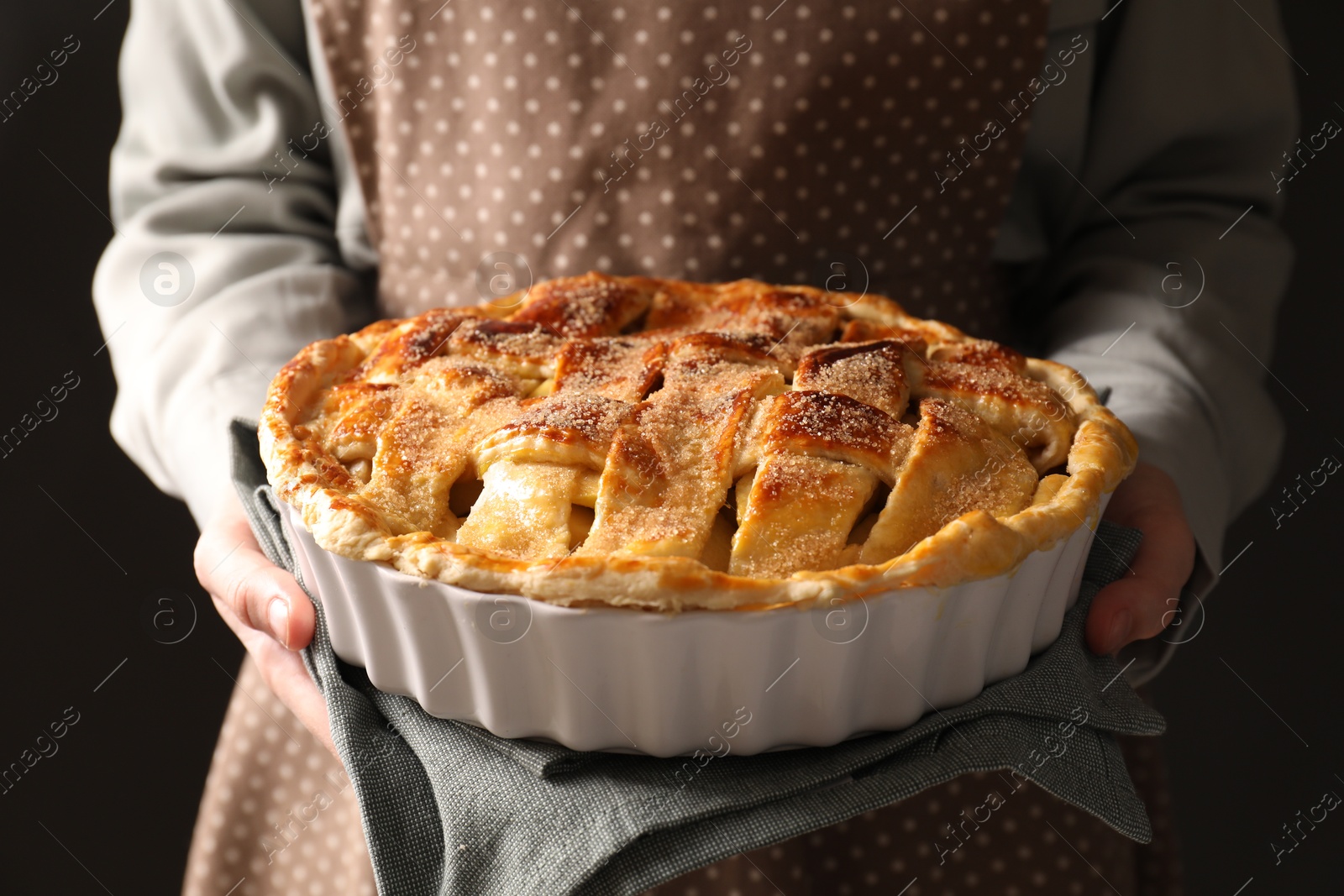 Photo of Woman holding tasty homemade apple pie on black background, closeup