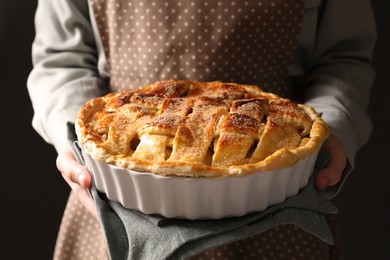 Woman holding tasty homemade apple pie on black background, closeup