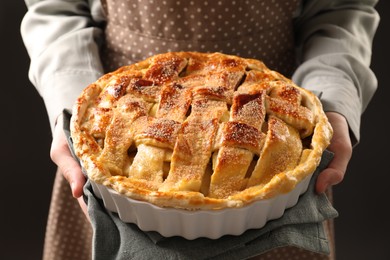 Woman holding tasty homemade apple pie on black background, closeup