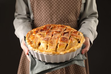 Photo of Woman holding tasty homemade apple pie on black background, closeup