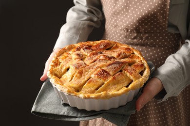 Photo of Woman holding tasty homemade apple pie on black background, closeup