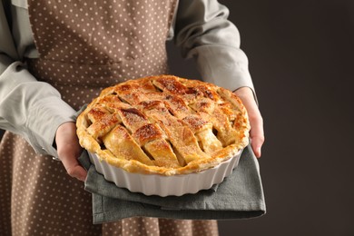 Photo of Woman holding tasty homemade apple pie on dark background, closeup