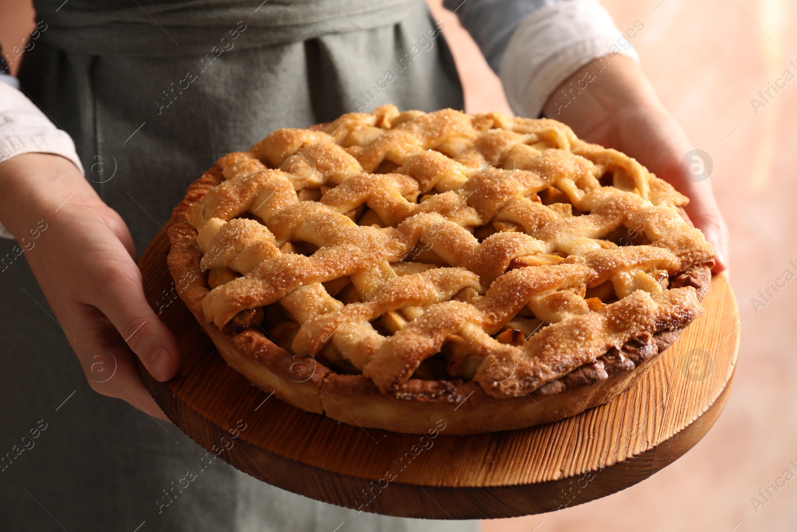 Photo of Woman holding wooden board with tasty homemade apple pie on light background, closeup