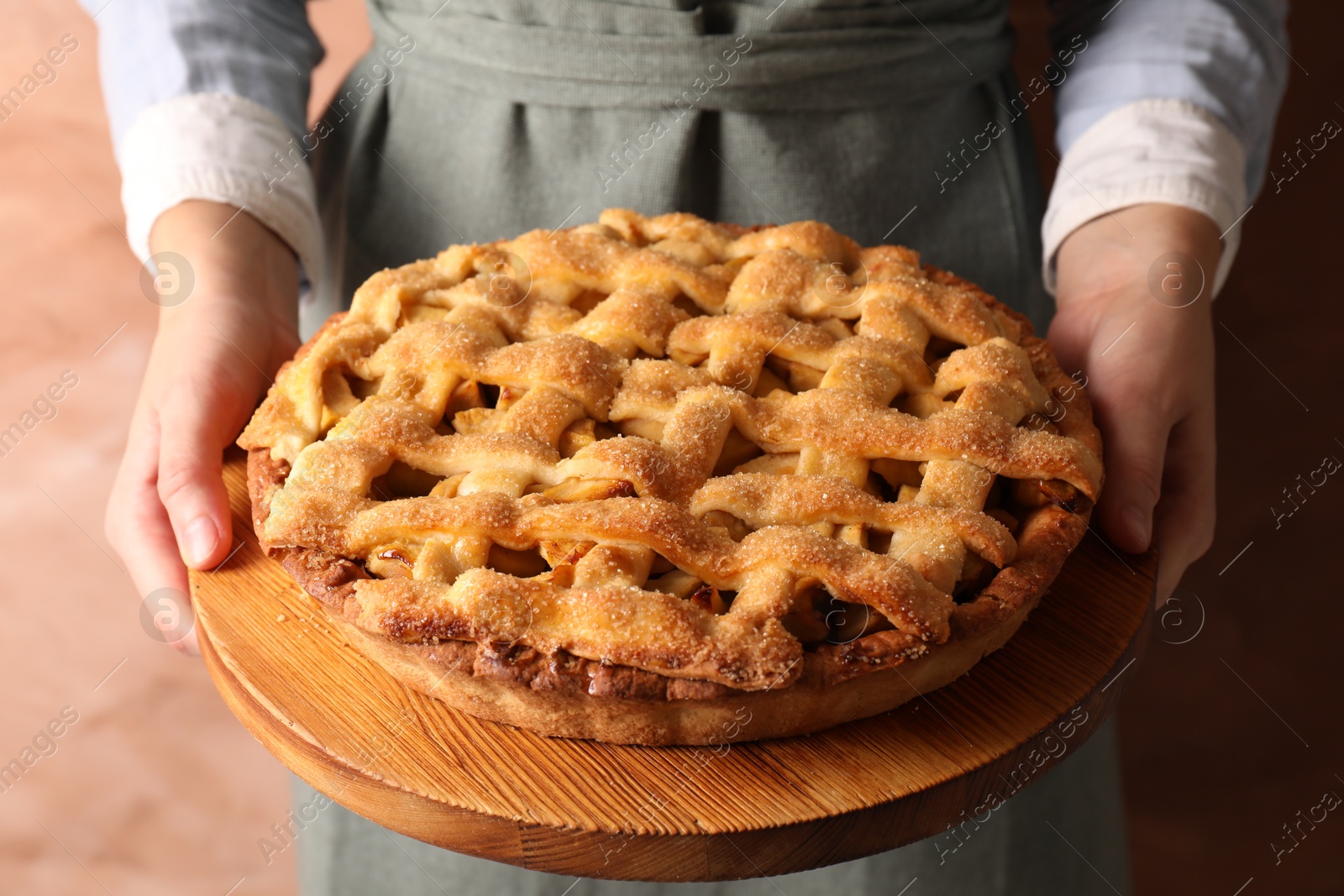 Photo of Woman holding wooden board with tasty homemade apple pie on light coral background, closeup