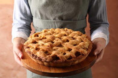 Photo of Woman holding wooden board with tasty homemade apple pie on light coral background, closeup