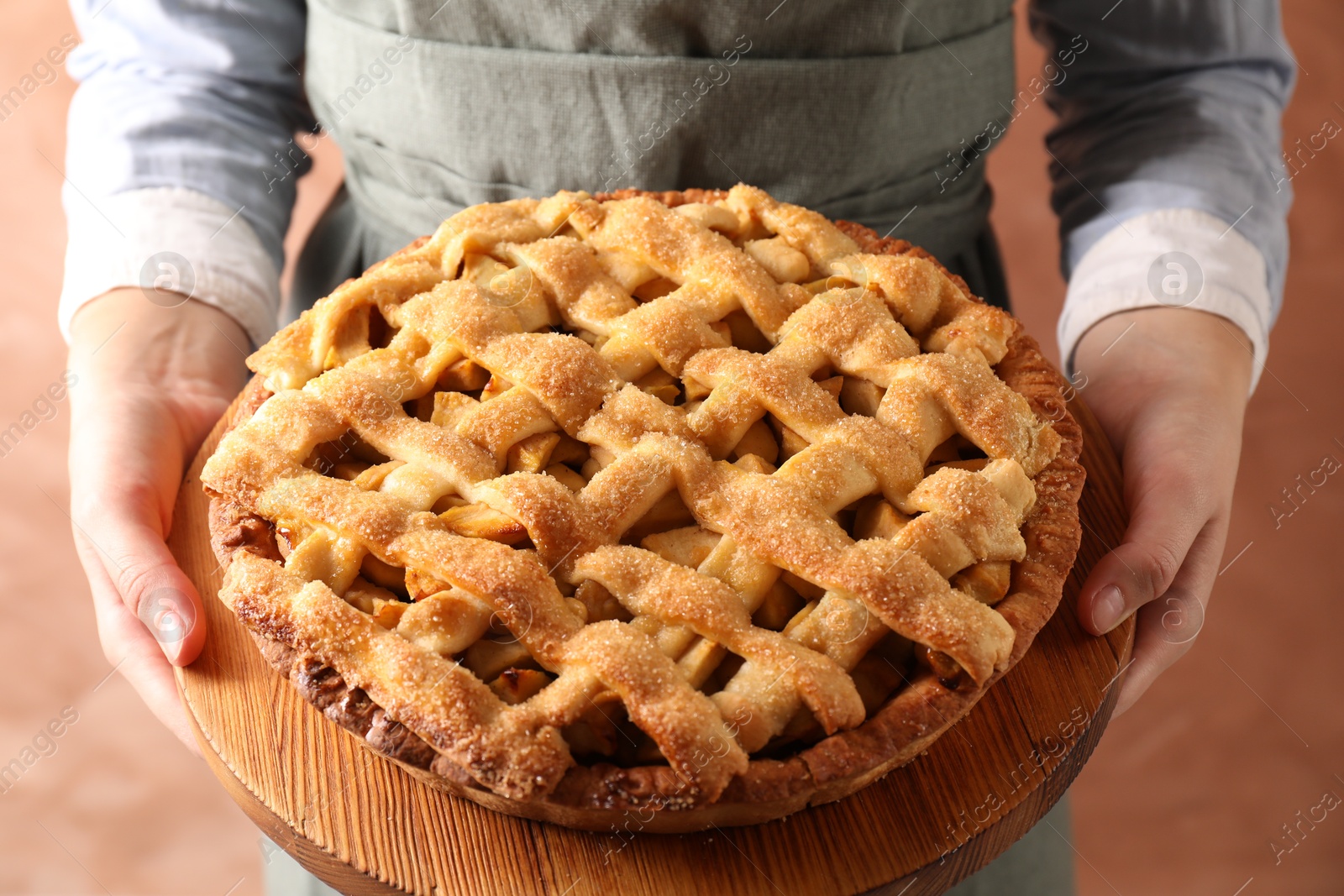 Photo of Woman holding wooden board with tasty homemade apple pie on light coral background, closeup