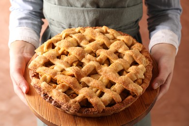 Photo of Woman holding wooden board with tasty homemade apple pie on light coral background, closeup