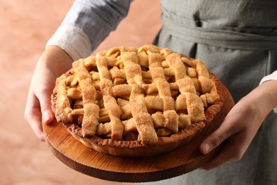 Woman holding wooden board with tasty homemade apple pie on light coral background, closeup