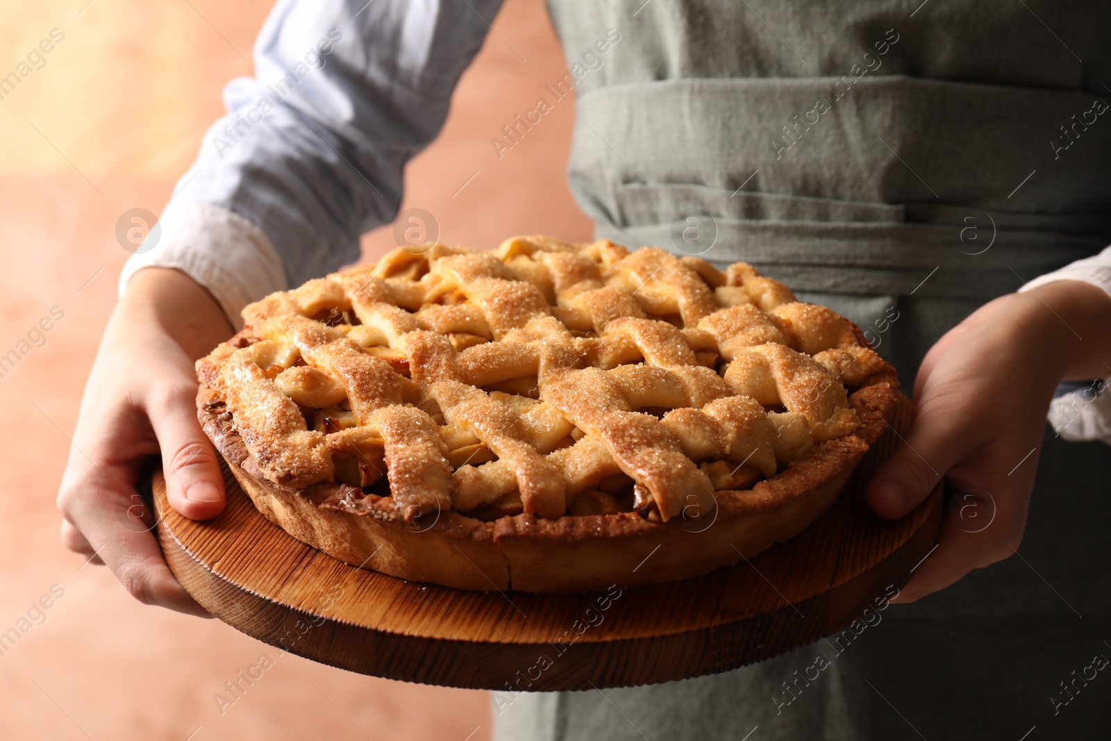 Photo of Woman holding wooden board with tasty homemade apple pie on light coral background, closeup