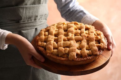 Woman holding wooden board with tasty homemade apple pie on light coral background, closeup