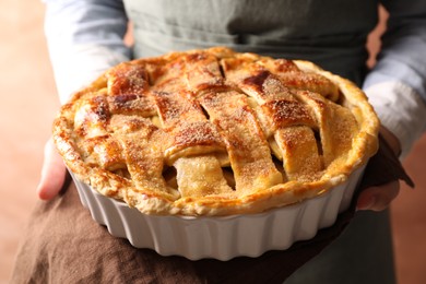 Woman holding tasty homemade apple pie on light coral background, closeup