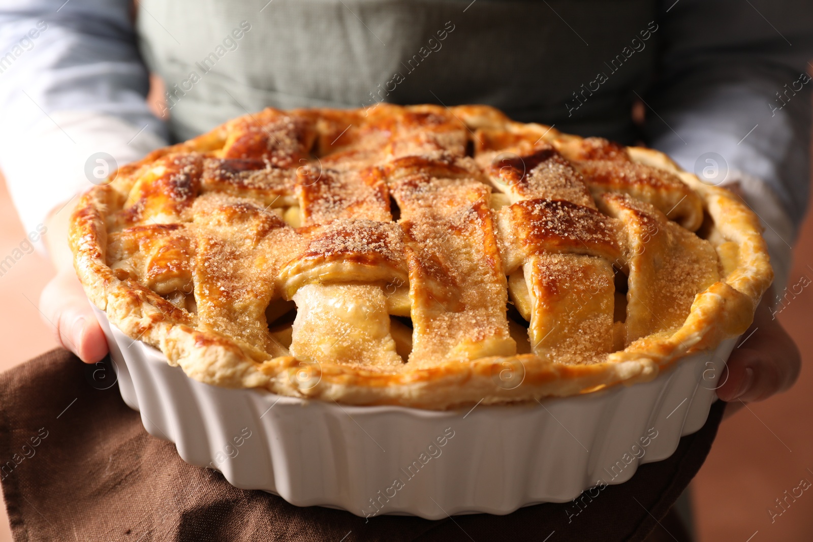 Photo of Woman holding tasty homemade apple pie on light coral background, closeup