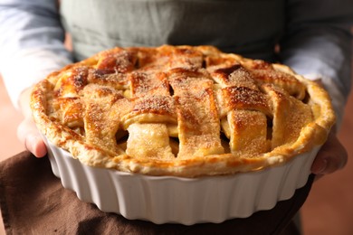 Woman holding tasty homemade apple pie on light coral background, closeup