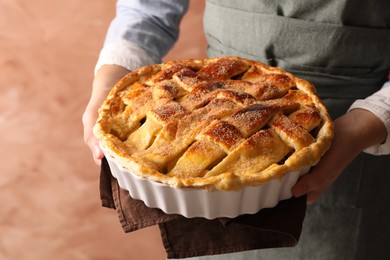 Woman holding tasty homemade apple pie on light coral background, closeup