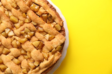 Photo of Tasty homemade apple pie on yellow background, top view. Space for text