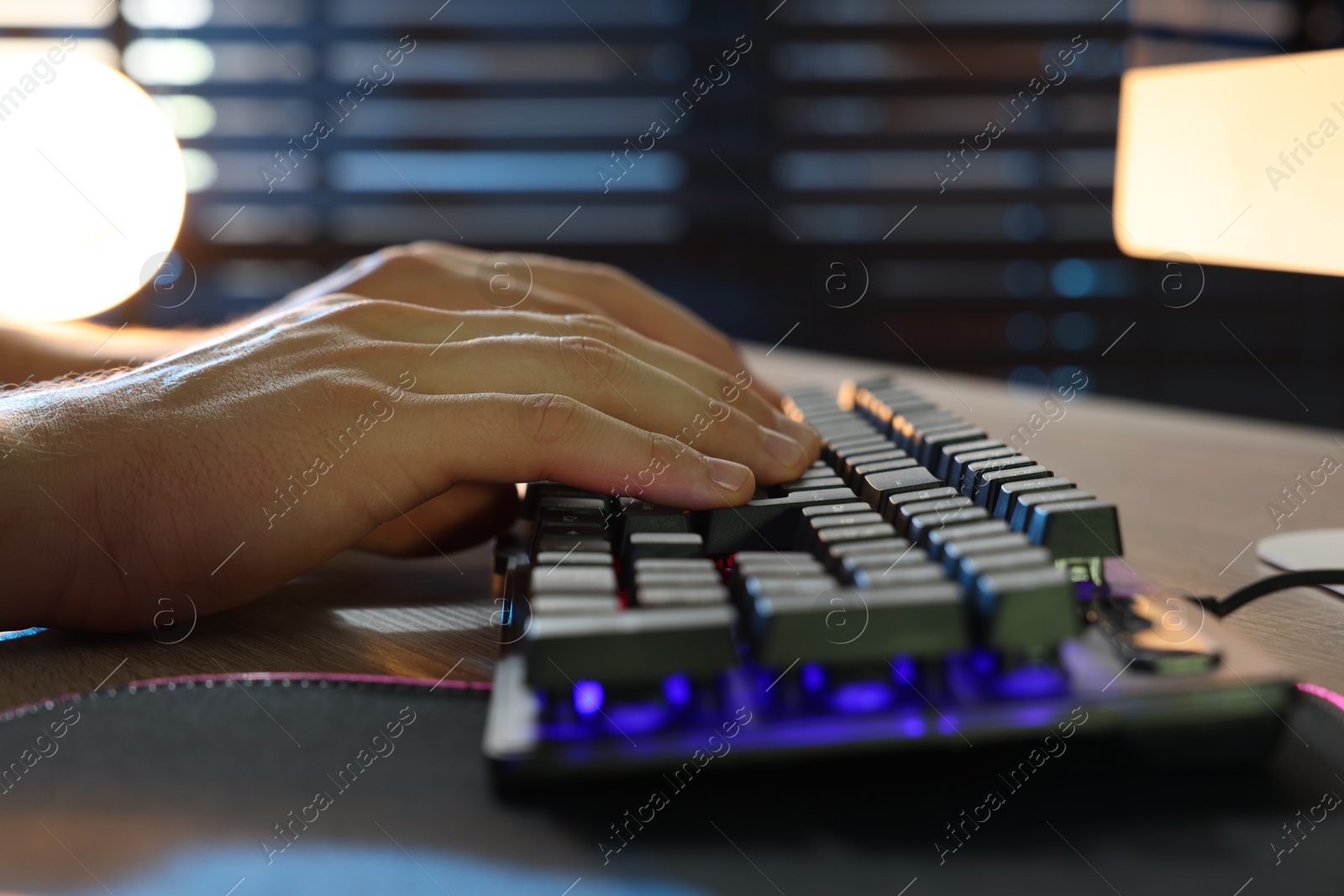 Photo of Young man using computer keyboard at wooden table indoors, closeup