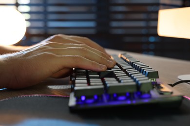 Photo of Young man using computer keyboard at wooden table indoors, closeup