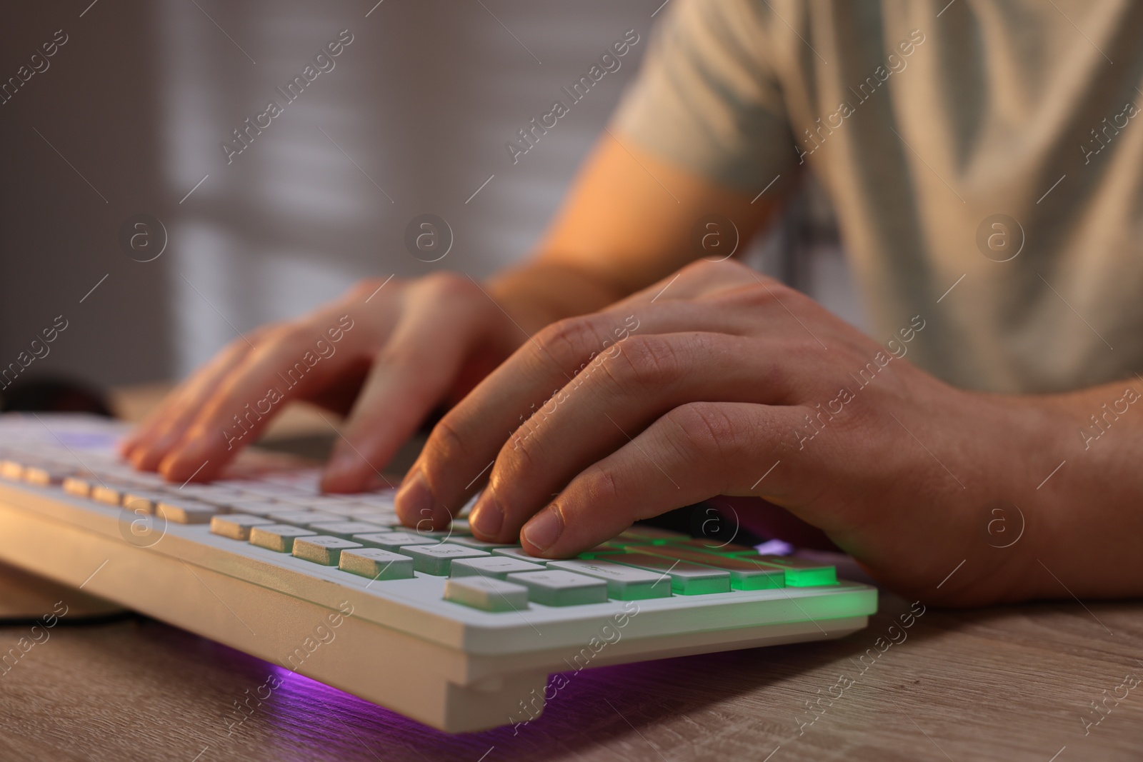 Photo of Young man using computer keyboard at wooden table indoors, closeup