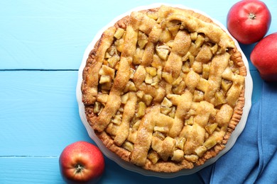 Photo of Homemade apple pie and apples on light blue wooden table, flat lay