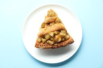 Slice of homemade apple pie on light blue background, top view