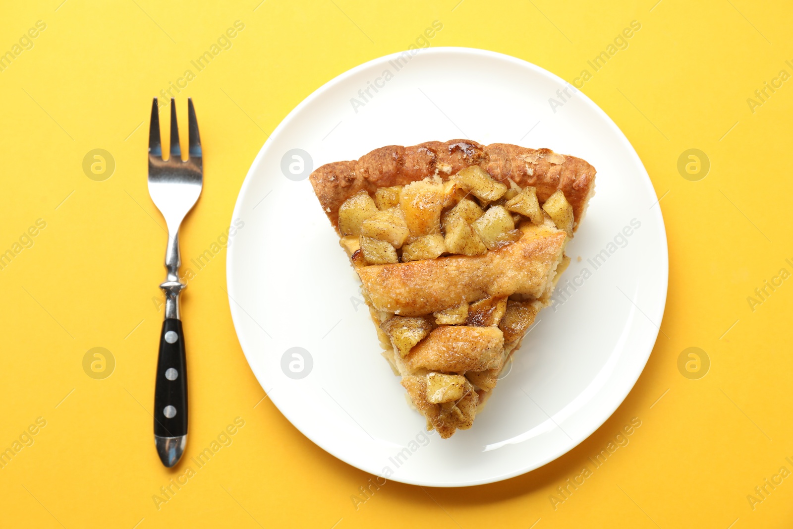 Photo of Slice of homemade apple pie and fork on orange background, top view