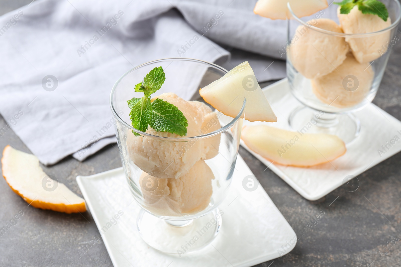 Photo of Scoops of melon sorbet with mint in glass dessert bowls and fresh fruit on grey table, closeup