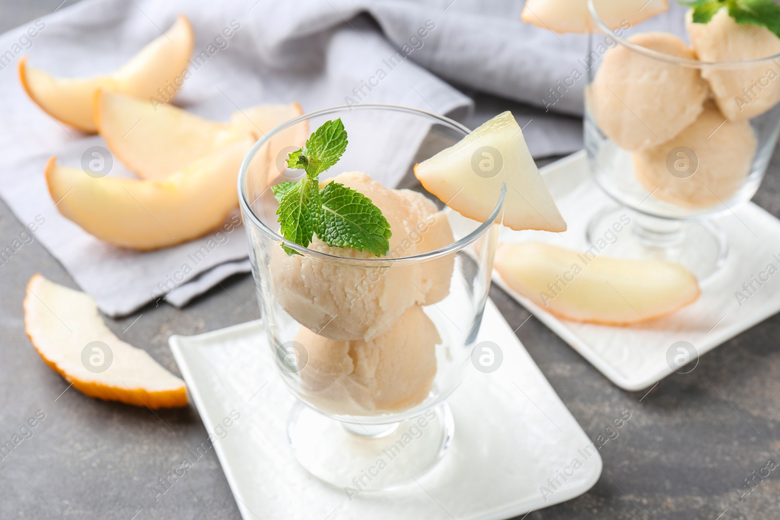 Photo of Scoops of melon sorbet with mint in glass dessert bowls and fresh fruit on grey table, closeup