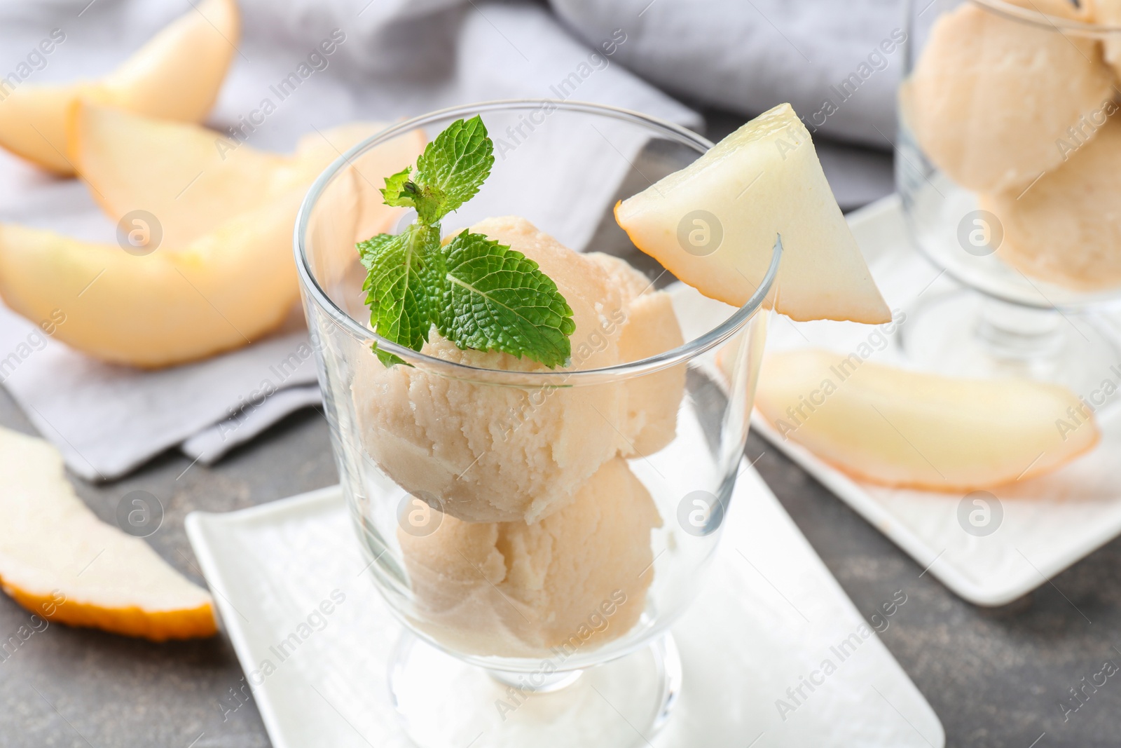 Photo of Scoops of melon sorbet with mint and fresh fruit in glass dessert bowl on grey table, closeup